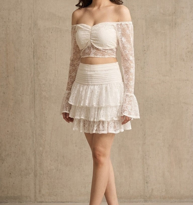 Woman wearing a white lace off-shoulder top and skirt against a neutral background